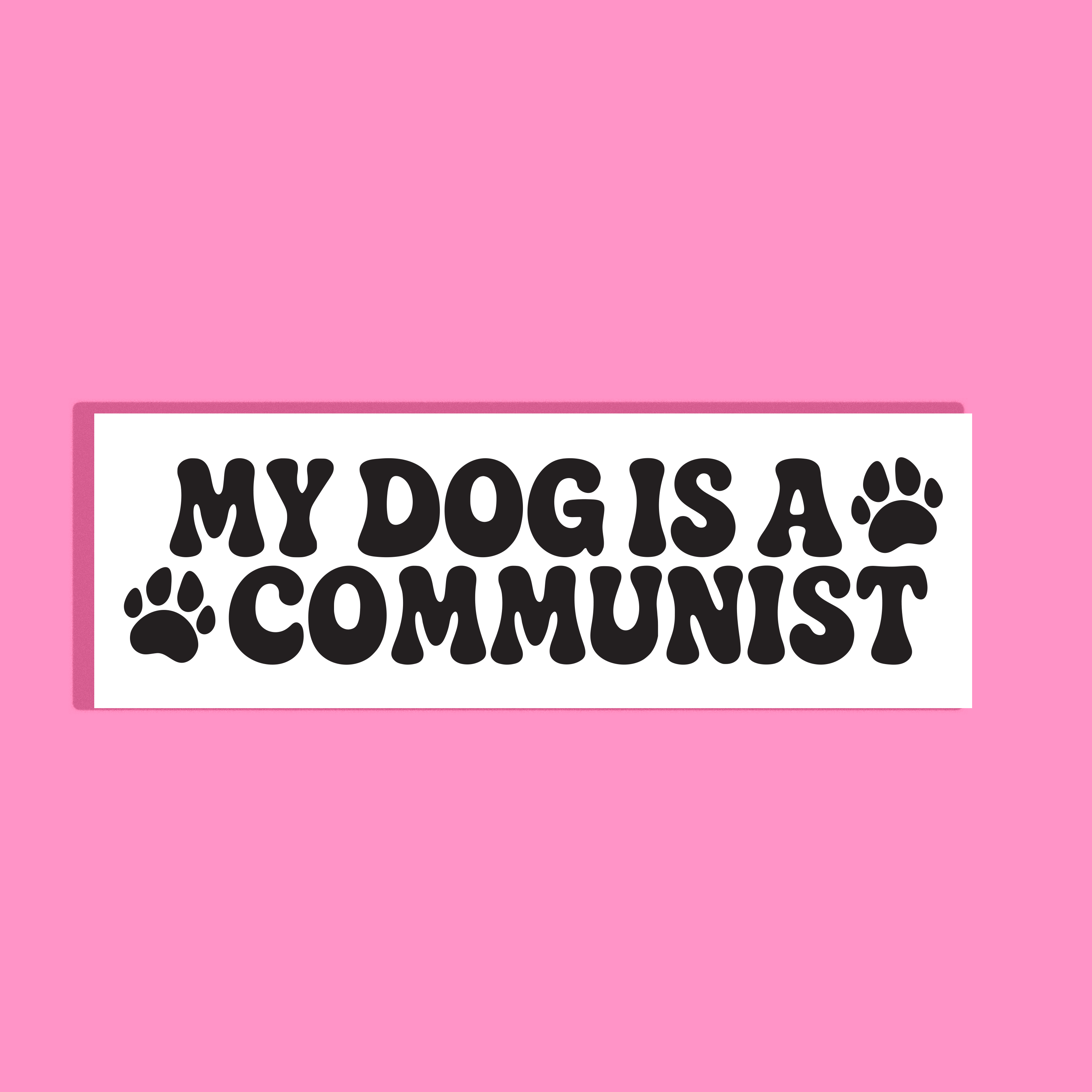 A rectangular white background with bold black text reading “MY DOG IS A COMMUNIST” and two black paw prints, shown on a solid pink background.