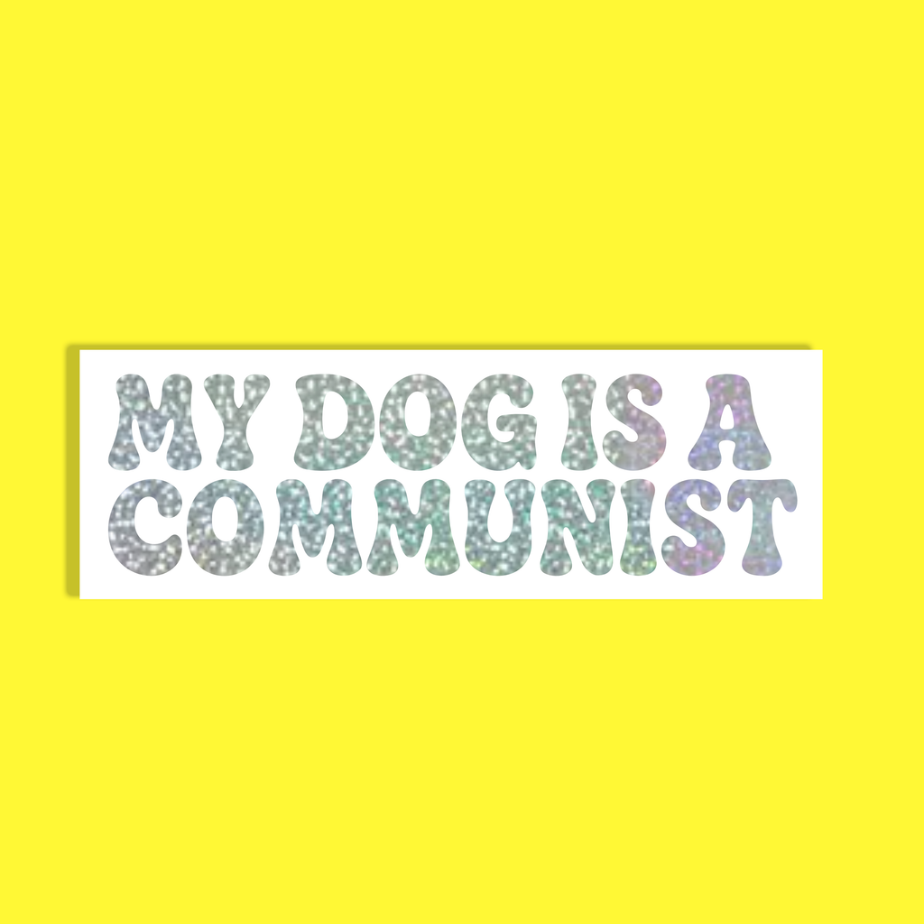 A rectangular white background with the text 'MY DOG IS A COMMUNIST' in a glittery, multicolored font, set against a solid bright yellow backdrop.