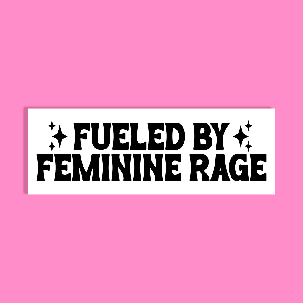 A white rectangle with bold black text reading 'FUELED BY FEMININE RAGE' accented with small starbursts, shown against a solid pink background.