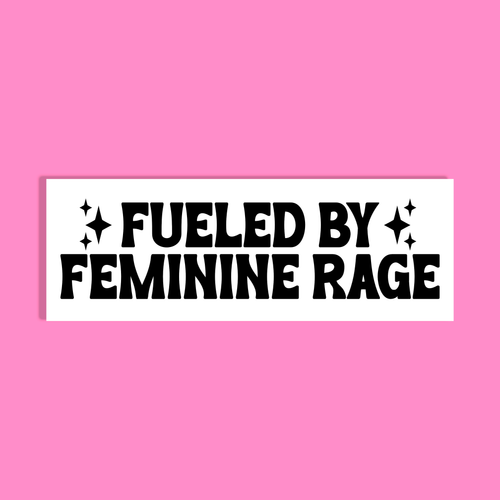 A white rectangle with bold black text reading 'FUELED BY FEMININE RAGE' accented with small starbursts, shown against a solid pink background.