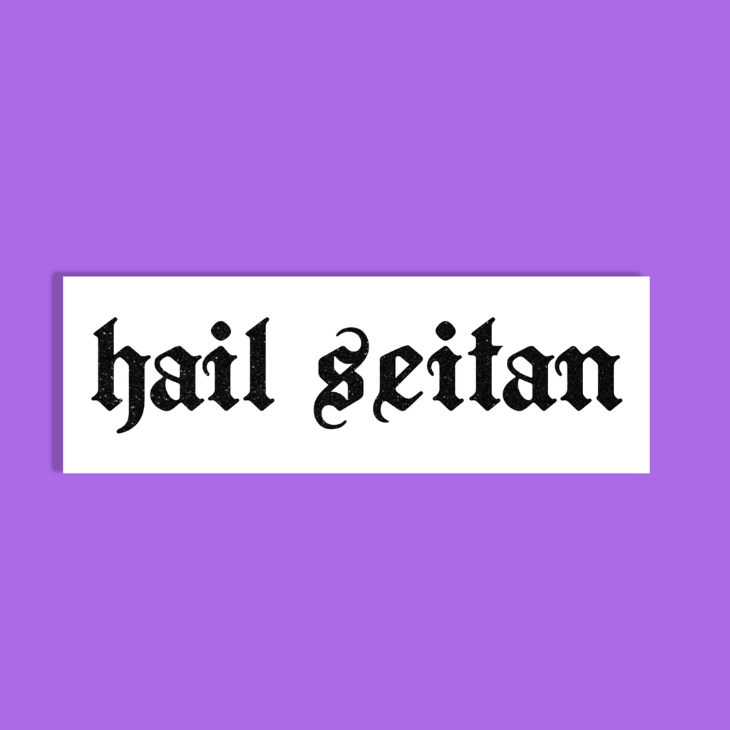 A white rectangular sticker or sign with the phrase 'hail seitan' in black gothic-style lettering, centered on a solid purple background.