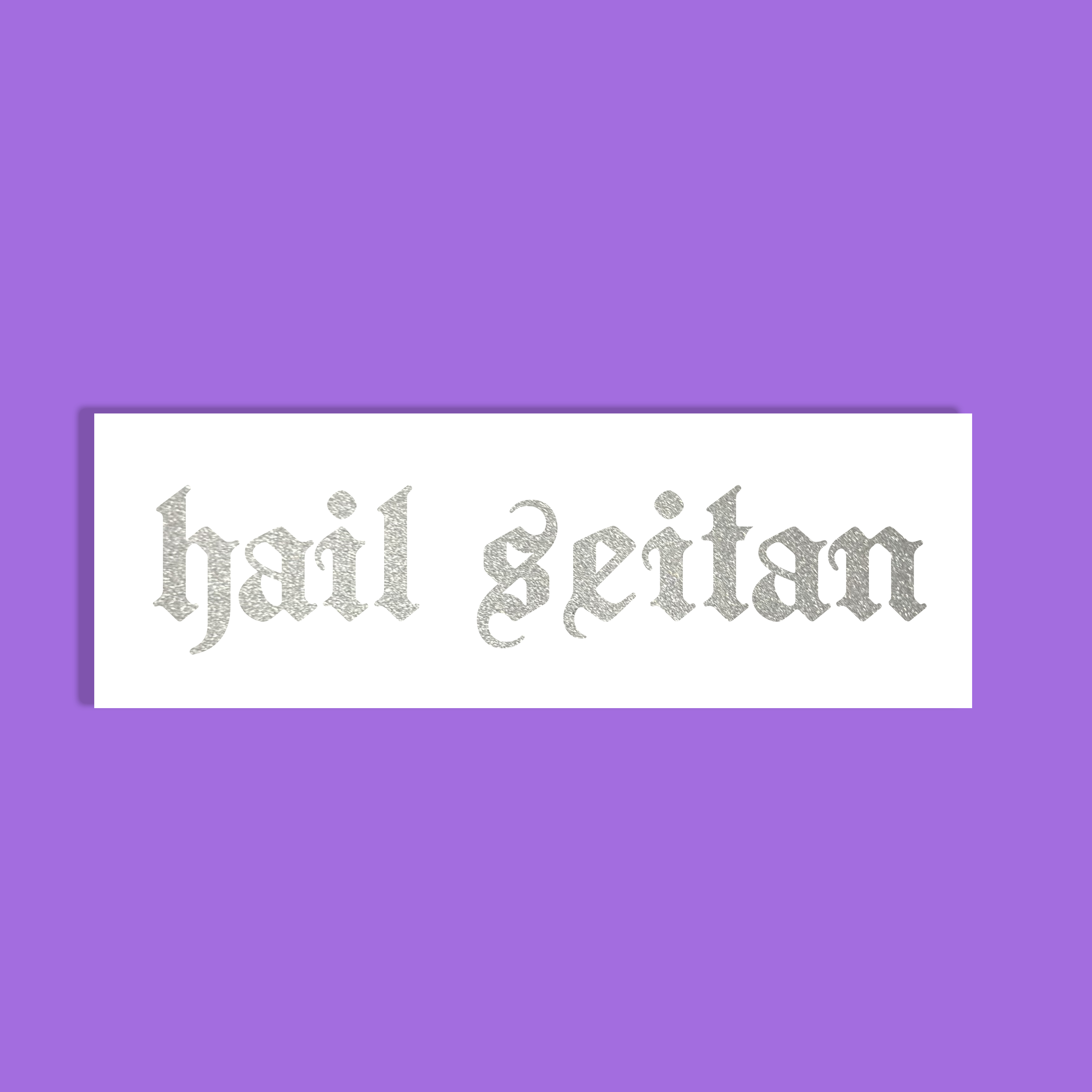 A rectangular white sticker or label with the phrase 'hail seitan' in a glittery silver gothic font, centered on a solid purple background.