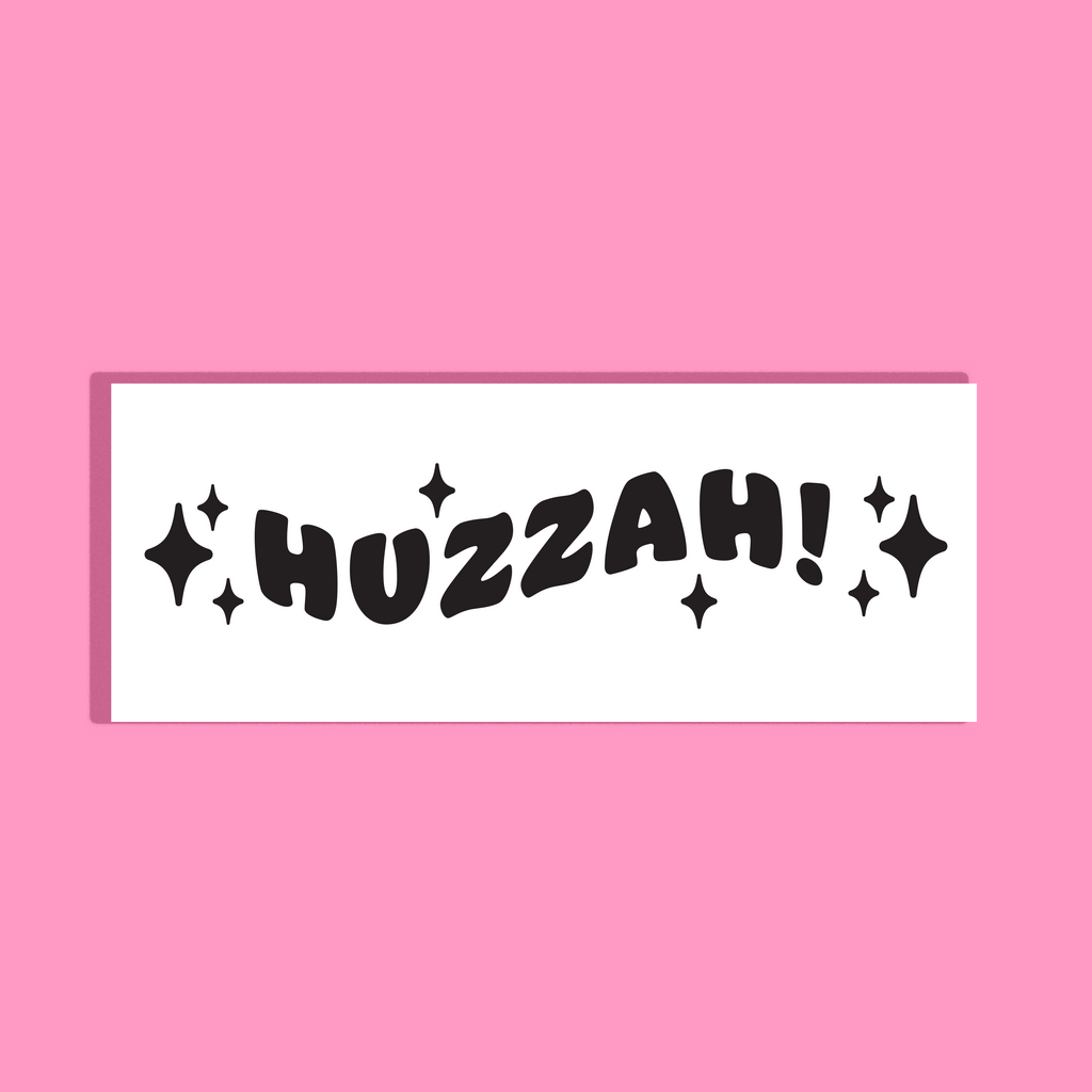A white rectangular background with the word 'HUZZAH!' in bold black bubbly letters and small black sparkle graphics, shown on a solid pink background.
