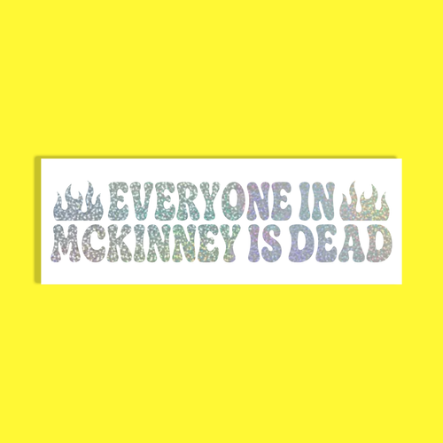 A rectangular white sticker with the text 'EVERYONE IN MCKINNEY IS DEAD' in a glittery, iridescent pastel font, flanked by two small flame icons, shown against a solid bright yellow background.
