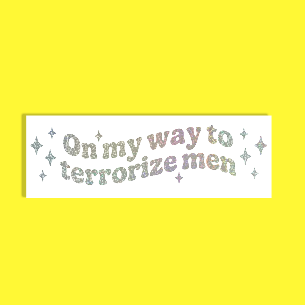A rectangular white background with the phrase 'On my way to terrorize men' in glittery pastel lettering, surrounded by small glittery stars, shown on a solid bright yellow background.
