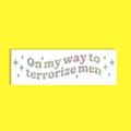A rectangular white background with the phrase 'On my way to terrorize men' in glittery pastel lettering, surrounded by small glittery stars, shown on a solid bright yellow background.
