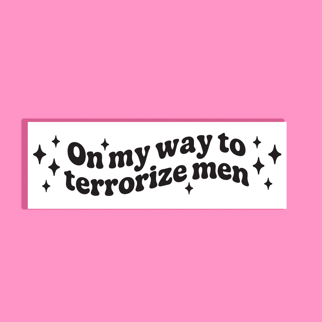 A white rectangular background with the phrase 'On my way to terrorize men' in black retro-style lettering, surrounded by small black sparkle graphics, shown on a solid pink background.