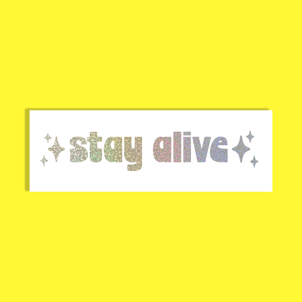 A rectangular white background with the phrase 'stay alive' in glittery multicolor letters, flanked by small glitter sparkles, shown on a solid bright yellow background.