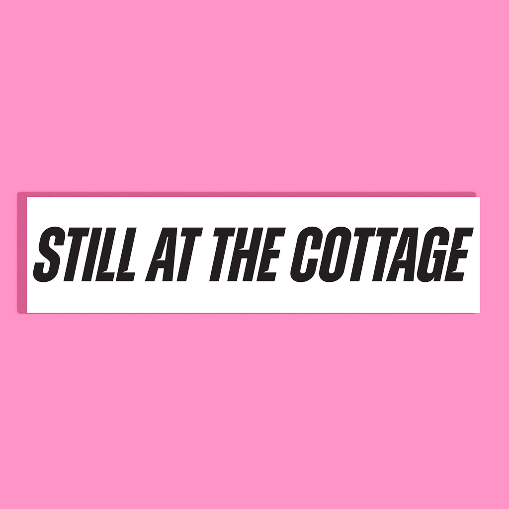 A rectangular white background with the phrase 'STILL AT THE COTTAGE' in bold black lettering, centered on a solid pink background.