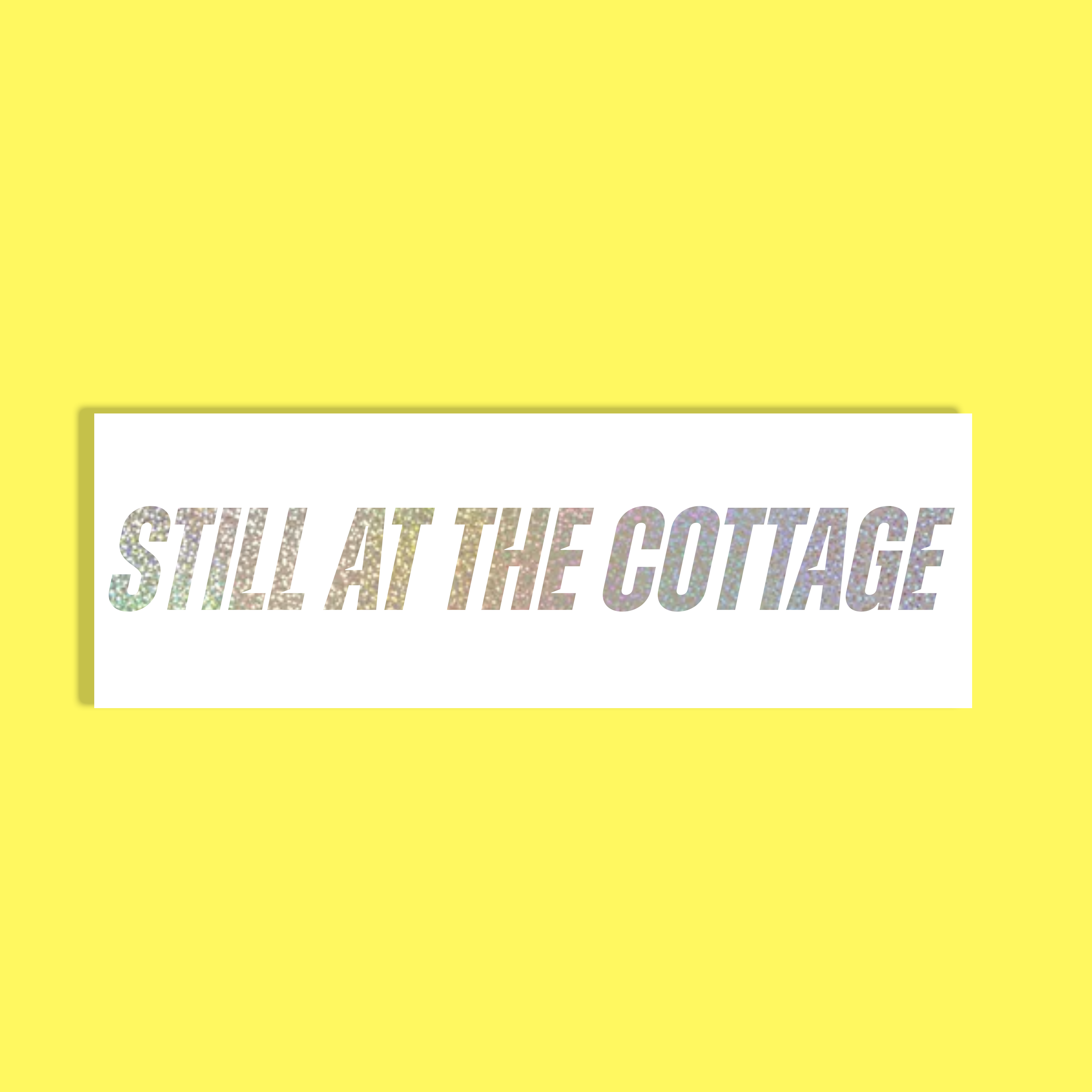 A rectangular white background with the phrase 'STILL AT THE COTTAGE' in silver glittery holographic letters, centered on a solid bright yellow background.